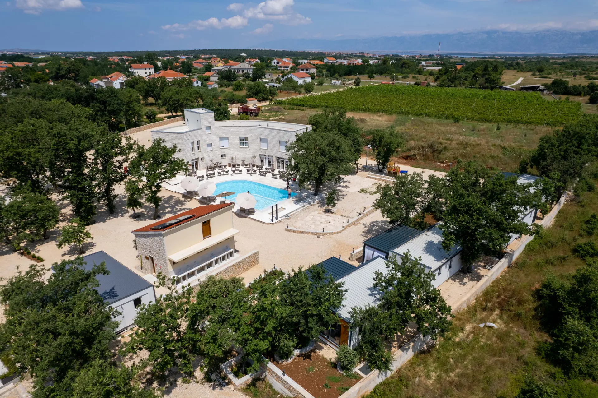 Ptičji pogled na kamp s bazenom u Zatonu, Kamp Dionis Zaton, Hrvatska. Kamp je okružen zelenim drvećem i ima čist plavi bazen.