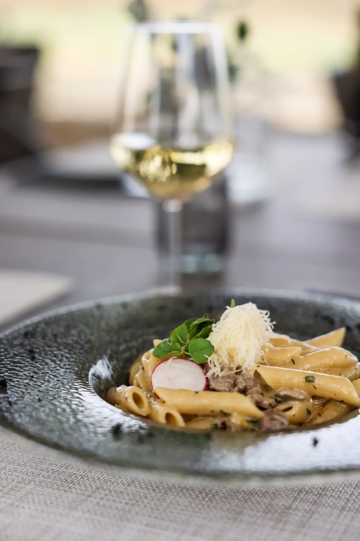 A plate of pasta, with aprmegano. There is also a glass of white wine.