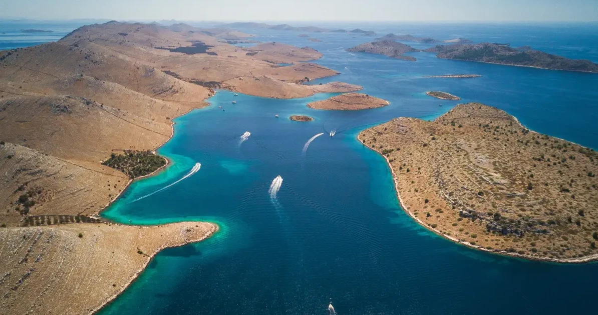 Luftansicht einer Gruppe von Inseln in der Adria. Die Inseln haben verschiedene Grüntöne und Blautöne, und es gibt mehrere Boote im Wasser. Dieses Bild stammt aus dem Nationalpark Kornati in Kroatien