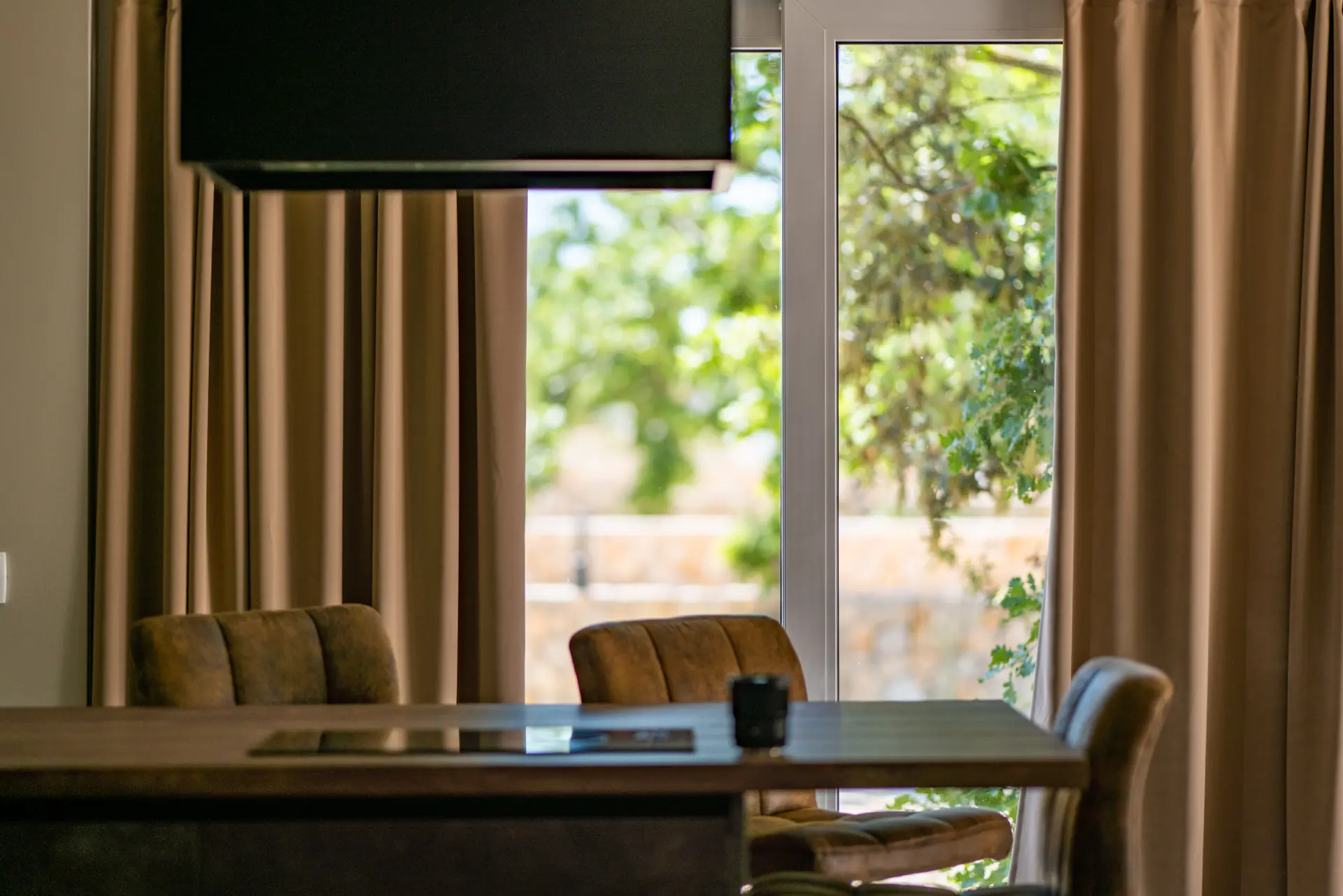 Kamp Dionis Zaton Mobile Home Premium. Udoban prostor za blagovanje s stolom, stolicama i pogledom prema van. Stol je od drveta, a stolice od pruća. Na stolu se nalazi vaza s cvijećem, a pogled kroz prozor pruža se na bujni zeleni vrt.
