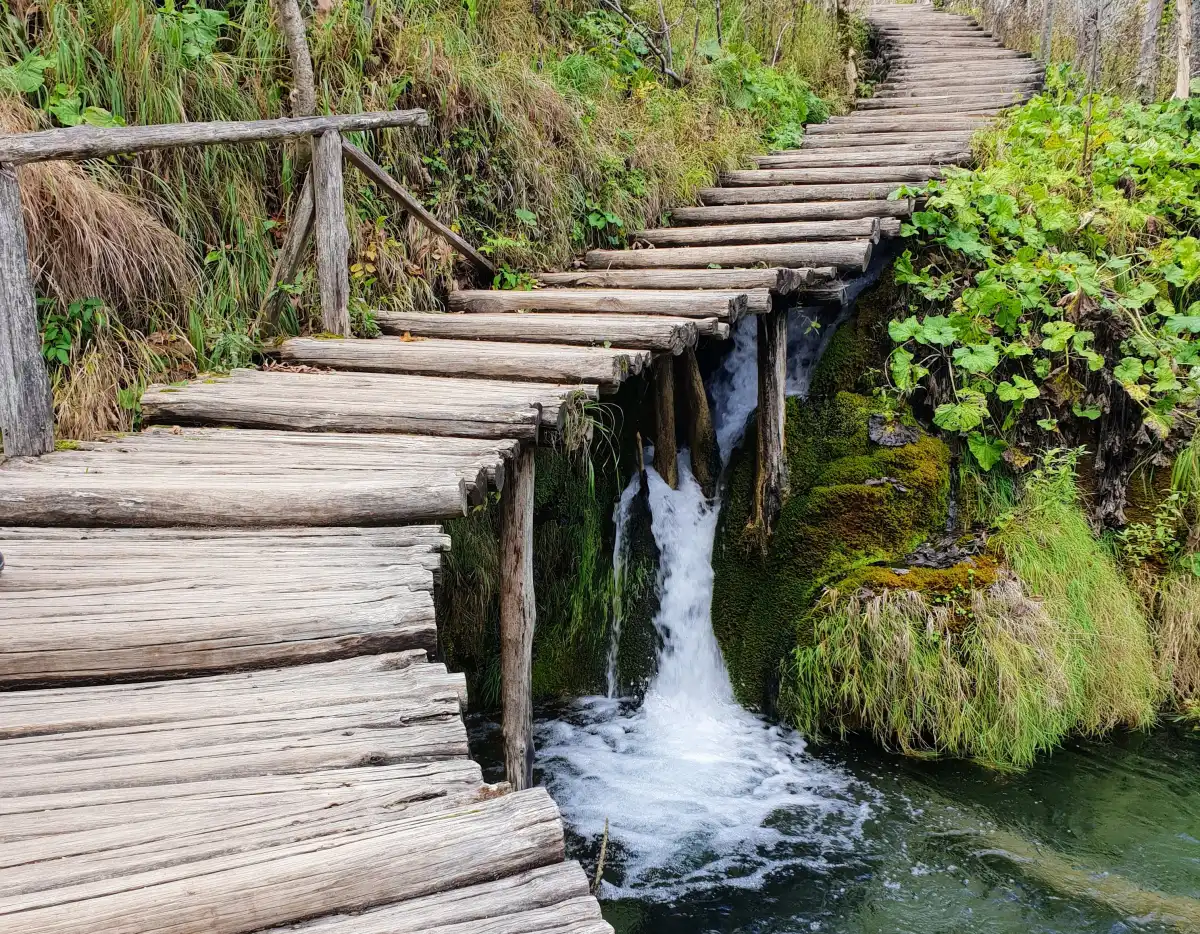 Ein hölzerner Weg, der zu einem Wasserfall im Wald des Nationalparks Plitvicer Seen in Kroatien führt